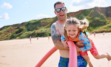 A Dad and daughter play together on the beach.
