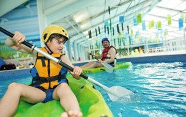 A child sat in a kayak paddling in the swimming pool