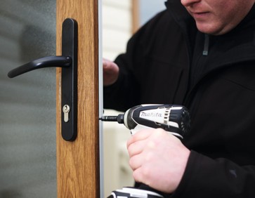 A member of park maintenance staff uses a drill to repair a caravan door.