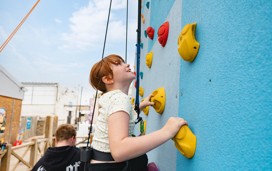 A little girl using the climbing wall at Haven's Blue Dolphin park