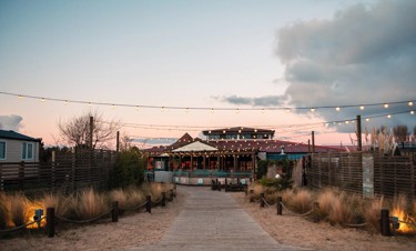 Twinkly lights festooned outside the Coast House restaurant at Seashore, with a pathway leading to the beach.