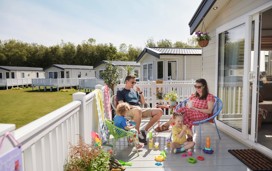 A family relax on the deck of their caravan in the sunshine.