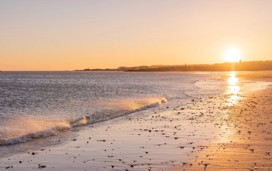 A view of sunrise and the waves crashing onto the shore at East Lothian's Golden Beaches in Scotland