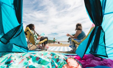 A couple sat down next to their tent with their kids playing in the background by the sea 